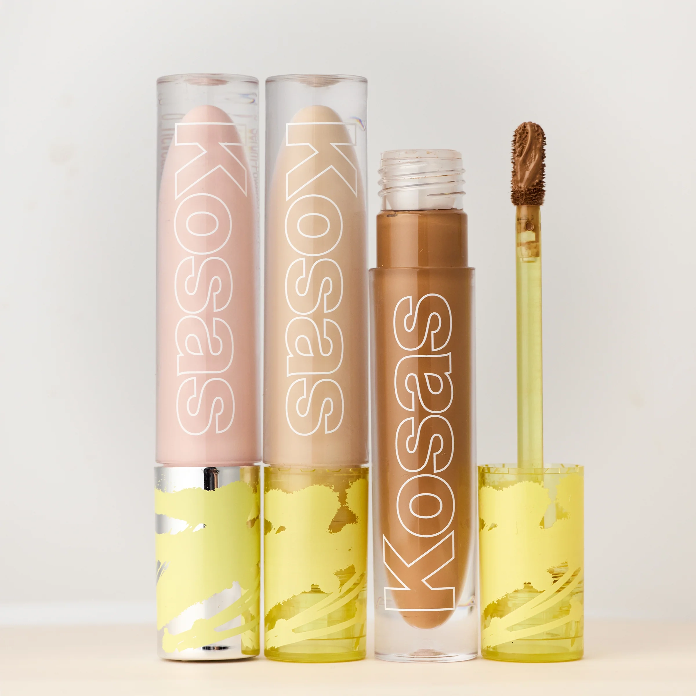 Two tinted concealers and a pot of balm beside a brown concealer wand